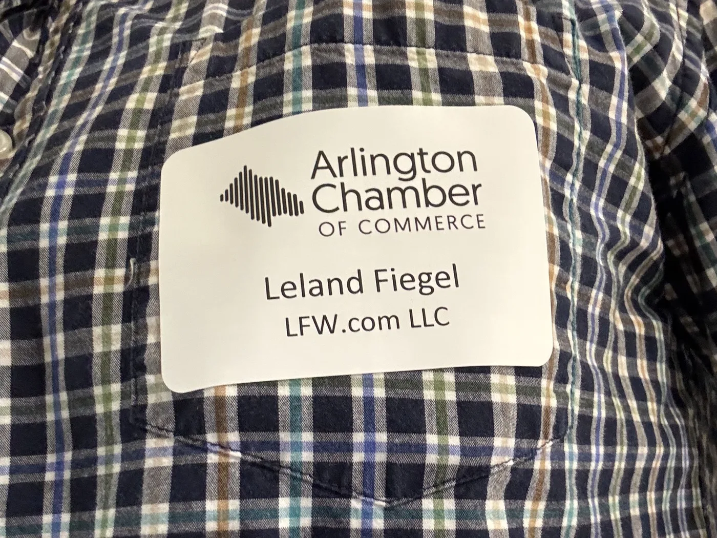 An Arlington Chamber of Commerce name tag reading Leland Fiegel, LFW.com LLC, stuck to the pocket of a plaid shirt.