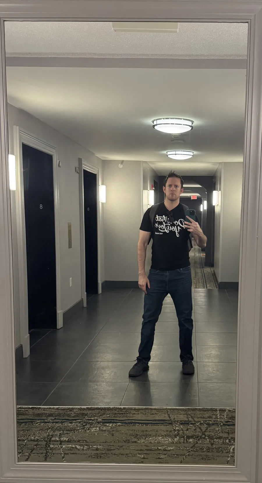 Leland in a hallway mirror wearing a black WeWork T-shirt that reads Do What You Love, with a backpack on.