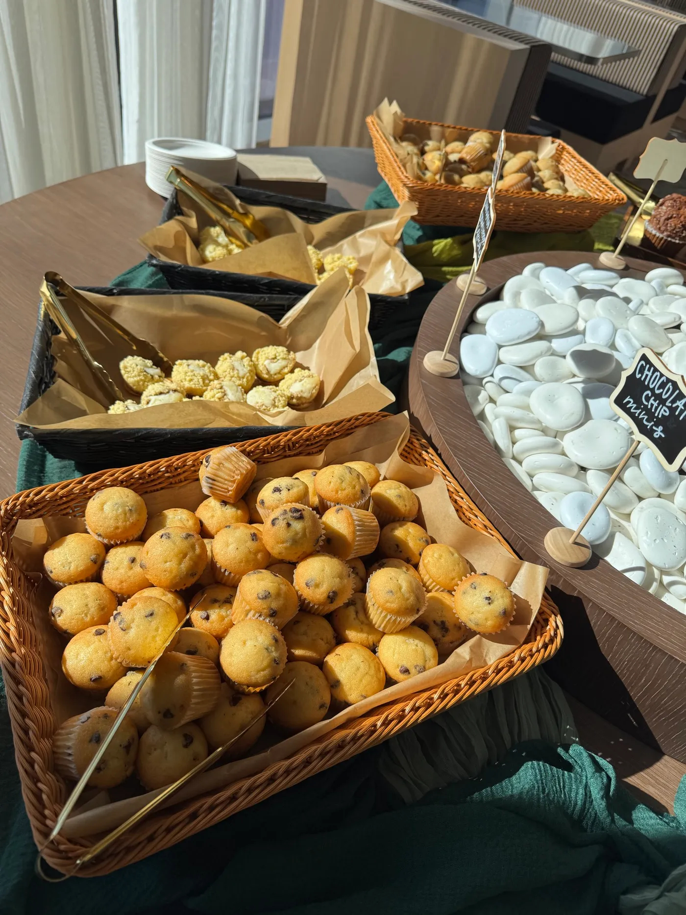 Cestini di mini muffin con pinze dorate al Mimosa Bar, mini muffin con gocce di cioccolato davanti e una piccola lavagna con scritto Chocolate chip minis.